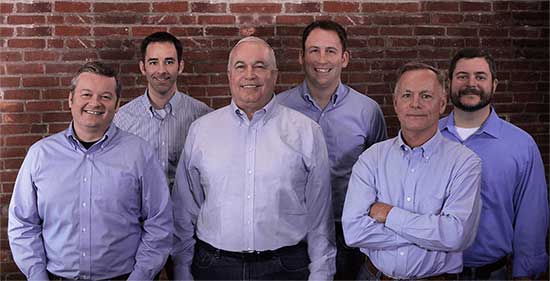 The attorneys of Edwards & Kautz in blue button-up long-sleeved shirts against a brick wall